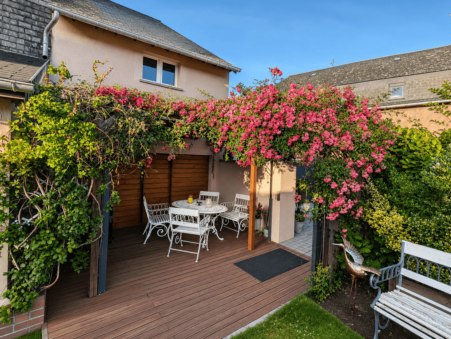 La terrasse de la maison, mobilier blanc sous une grimpante en fleurs