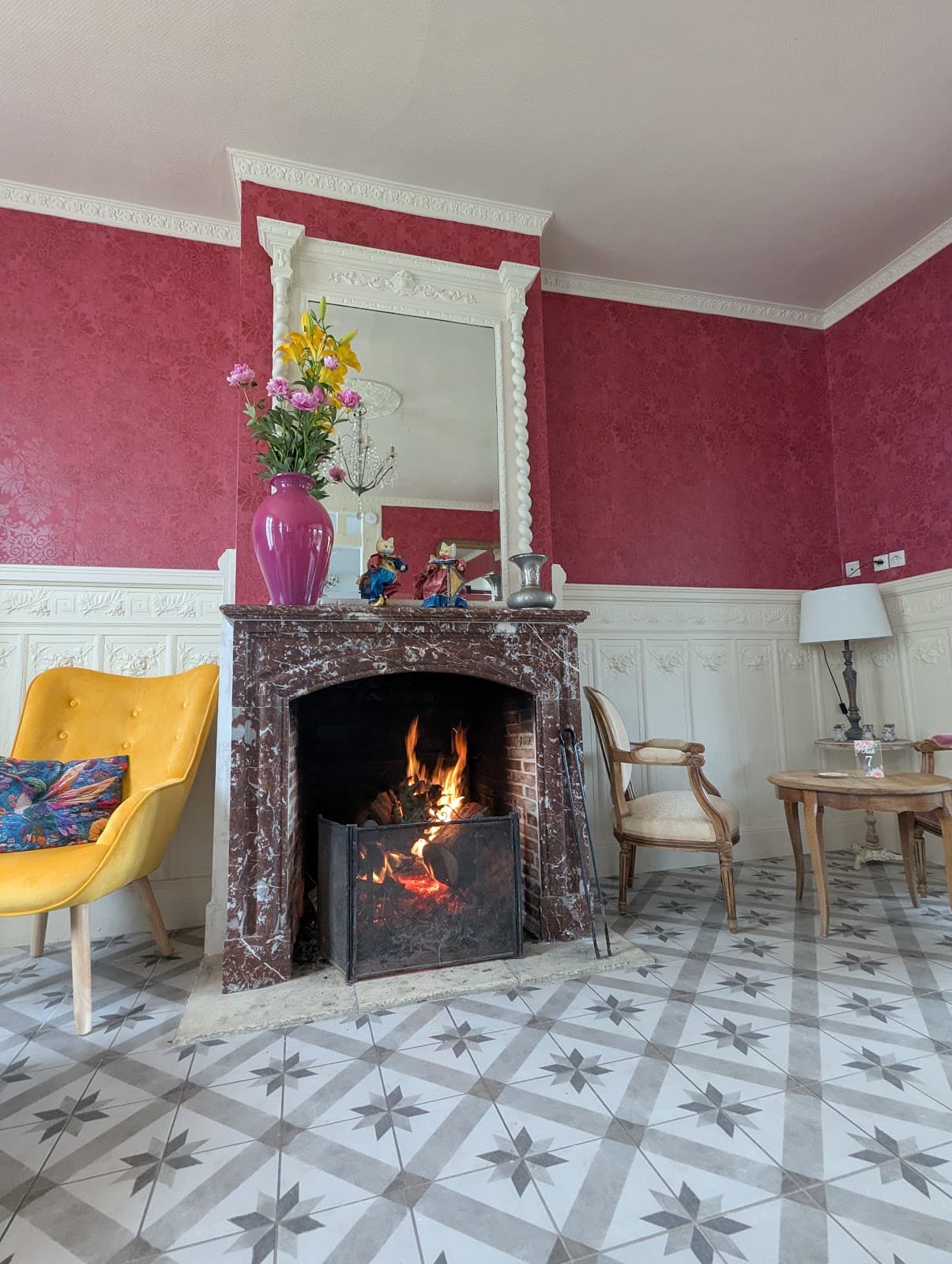Le salon, sa cheminée, ses murs rouges et un fauteuil jaune moutarde