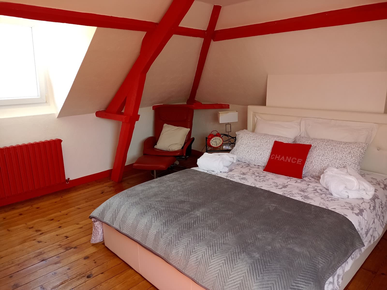 Chambre mansardée, lit blanc et poutres rouges apparentes