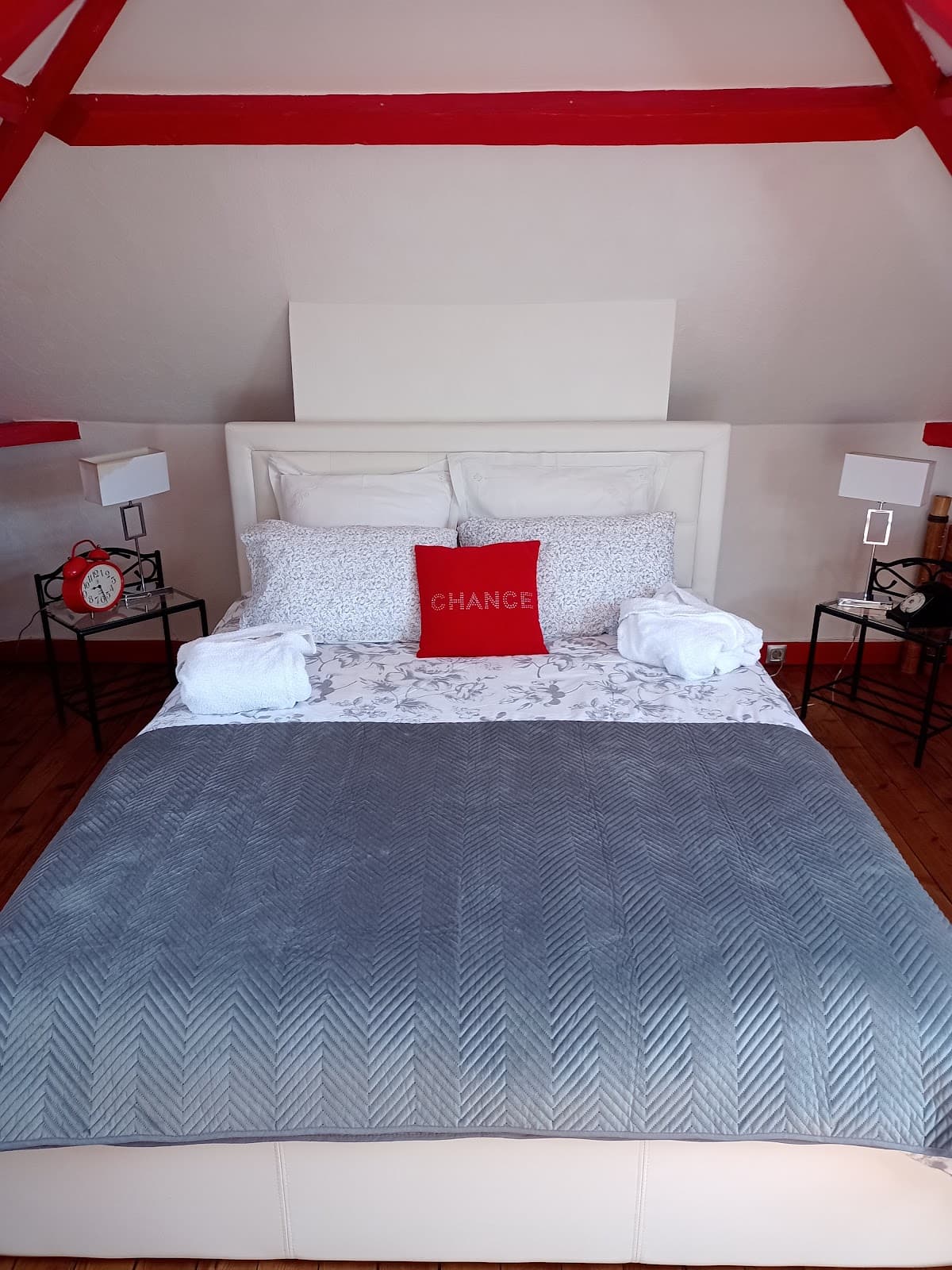 Vue depuis le lit, coussins rouges et blancs sous les poutres