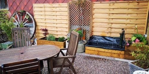 Table ronde de bois et chaises dans la cour, entourées de jardinières