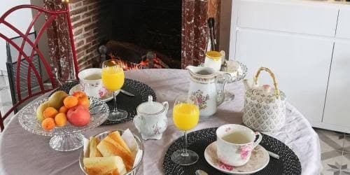 Table du petit déjeuner dressée : théière, oranges et croissants, cheminée en arrière-plan